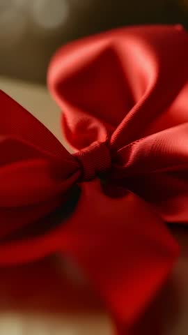 Vertical video pulling focus to red satin bow tied on gift with yellow tag and soft bokeh