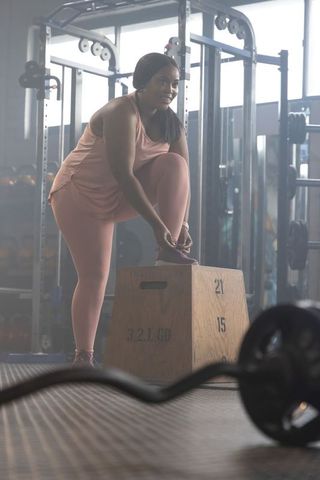 African american woman tying shoe on plyo box in gym preparing for strength training