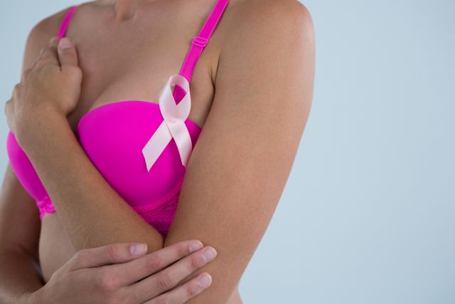 Woman with Breast Cancer Awareness ribbon touching hand while standing against gray background