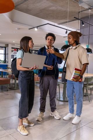 College students collaborating in modern campus lounge with laptop, notebooks, headphones