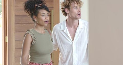 Diverse young couple reacting with surprise while entering bright wood-panel foyer