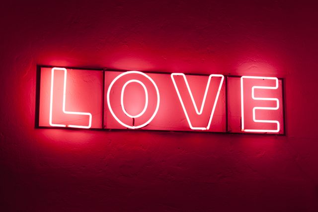 Pink neon love sign glowing on dark background. Perfect for themes of romance, intimate settings, and holiday decorations such as Valentine's Day. Ideal for use in designing greeting cards, posters, social media posts, and event invitations.