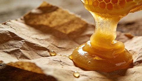 Golden honey pouring from honeycomb onto kraft paper macro close-up glossy amber drizzle