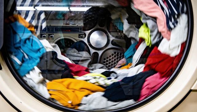 Colorful clothes tumbling inside front-loading washer door spinning drum, vibrant apparel