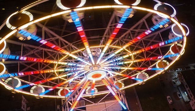 Spinning neon ferris wheel creating rainbow led light trails over urban night parking