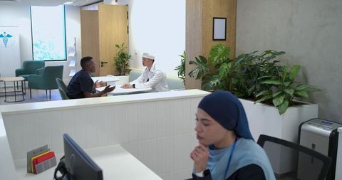 Diverse clinic team consulting patient at modern reception desk with plants and calm vibe