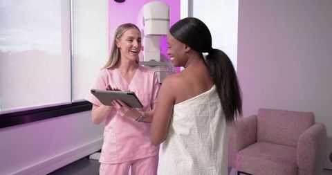 Healthcare technician consulting with Black patient before mammogram in pink clinic