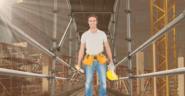 A male construction worker is standing confidently on scaffolding while holding a yellow hard hat. He is smiling and equipped with safety tools, emphasizing workplace safety and professionalism. Ideal for advertisements or articles about construction, safety at work, and building practices.