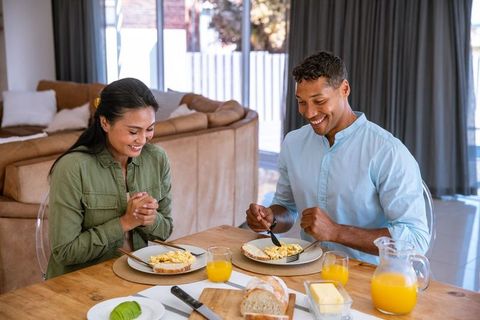 Diverse couple enjoys cozy breakfast at home with scrambled eggs and orange juice