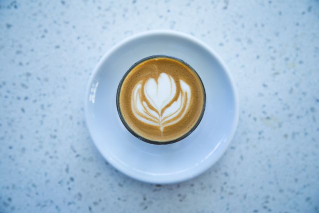 Top view of a beautiful latte art design in a white cup on a marble table is exhibited. Ideal for cafe menus, coffee culture articles, barista skill features, or social media posts related to coffee appreciation.