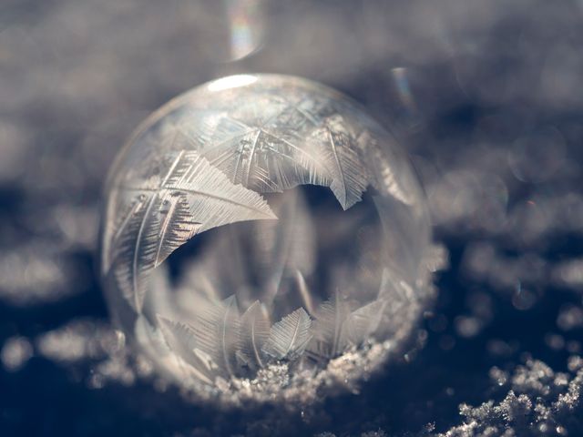This close-up shot captures the delicate beauty of a frozen soap bubble adorned with detailed frost patterns, nestled on a bed of snow. The intricate ice crystals showcase the symmetry and complexity of natural freeze formation. Ideal for seasonal advertisements, nature photography collections, educational purposes highlighting physical sciences, or holiday-themed decorations emphasizing the winter aesthetic.