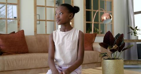 Young african american girl sitting on coffee table gazing thoughtfully in contemporary living room