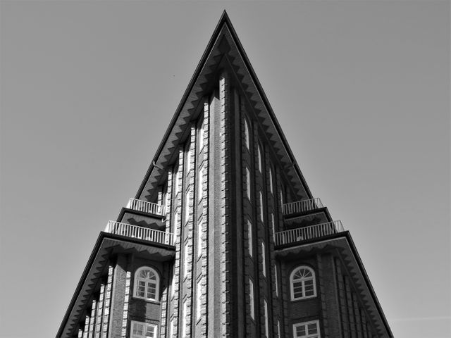 Black and white view of a high-rise building with sharp angles, featuring geometric shapes and arched windows. Useful for architectural design studies, urban planning, modern cityscapes, or illustrating contemporary architecture theories.