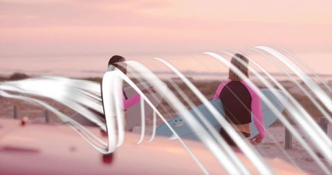 Surfers holding boards enjoying pastel sunset on sandy beach