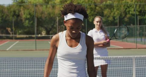 African American tennis player standing at net with focused expression and opponent behind