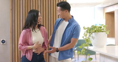 Hispanic and asian couple laughing and talking in modern reception lounge
