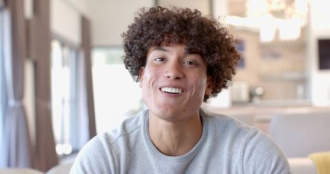 Smiling young man sitting in sunlit modern home headshot wearing casual gray sweater cozy