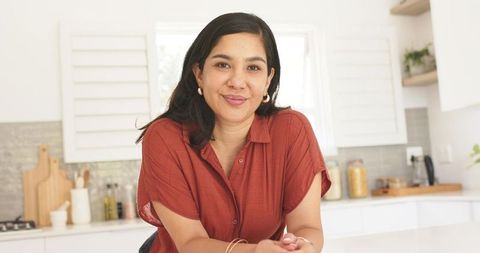 Leaning smiling woman on kitchen countertop wearing rust shirt in minimalist modern home