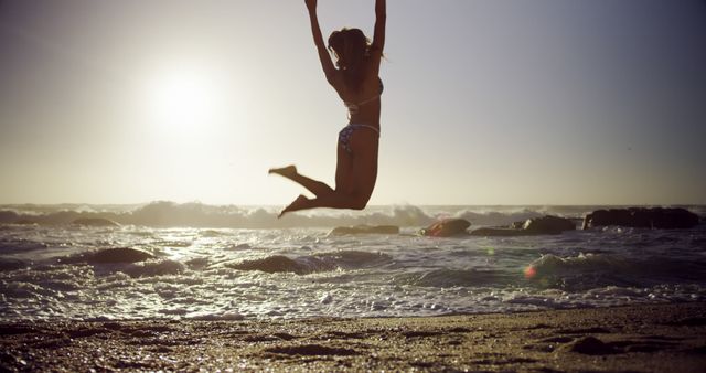 Silhouetted person jumps joyfully on a sunny beach. Capturing the essence of freedom and happiness, the image evokes a sense of carefree summer days.