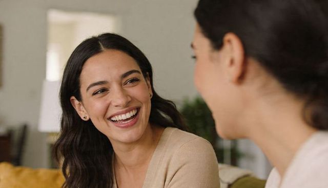 Smiling woman sharing warm, genuine conversation with friend on couch in cozy living room