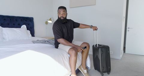 Man ready for travel in modern bedroom holding rolled luggage