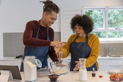 Couple cracking eggs and whisking batter at kitchen island, joyful home baking moment
