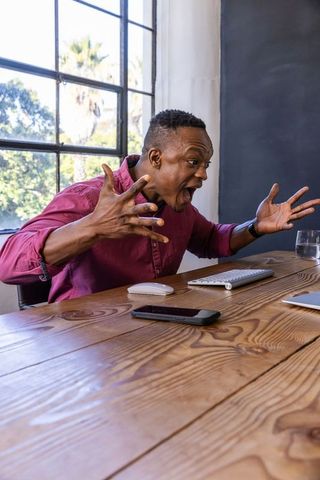 Frustrated man in home office lifting hands with laptop nearby