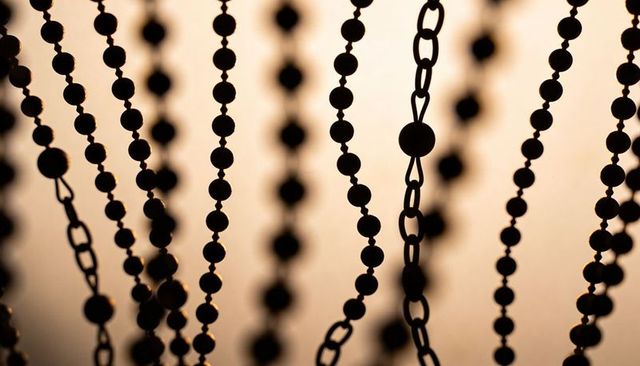 Silhouetted hanging bead chains with warm sunset backlight, amber bokeh and metal loops