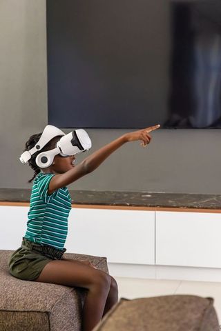 Young african girl wearing vr headset pointing and exploring virtual reality at home