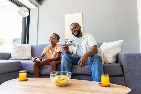 African american father and son playing video games on sofa bonding at home