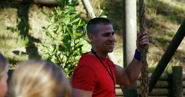 Man guiding participants in outdoor fitness activity holding a rope, ideal for articles on fitness coaching, outdoor workout routines, group training, healthy lifestyles, sports camps, or leadership and teamwork exercises.