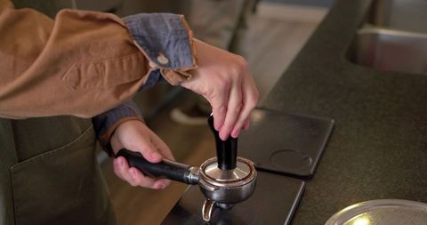 Barista tamping espresso into portafilter on stainless counter closeup rustic cafe