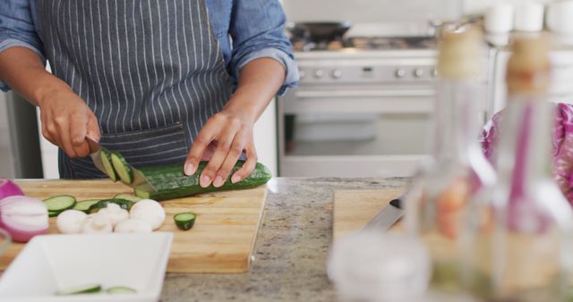 Image of midsection of caucasian man cutting cucumber in kitchen. Lifestyle, cooking, household and spending time at home concept.