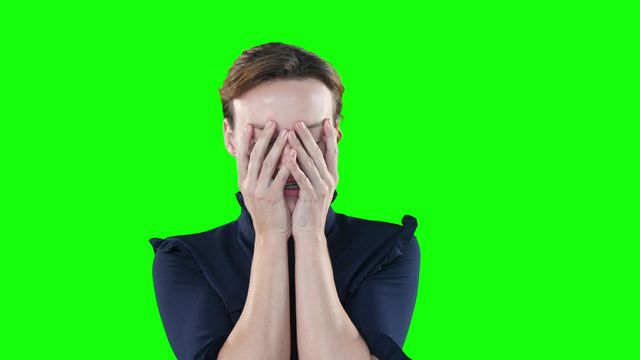 Angry attractive Caucasian woman with brown hair, wearing black blouse, screaming, cursing and flicking her hands on green background.