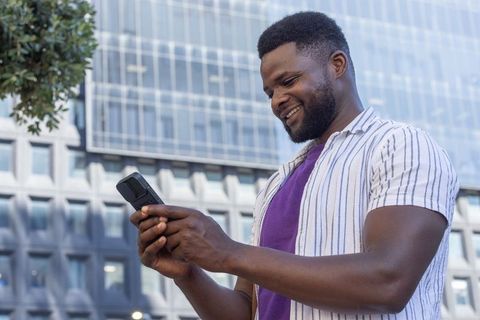 African american man smiling and texting on smartphone in urban high-rise business area