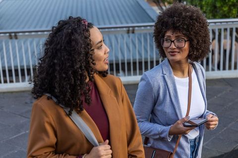 Two african american women walking and talking on urban pedestrian bridge in blazers
