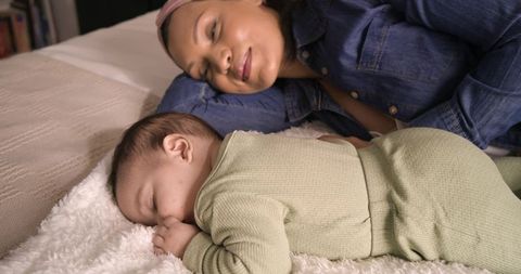 Mom Resting alongside Baby on Cozy Bed with White Blanket