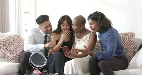 Diverse friends sharing smartphone and reacting with surprise on sofa